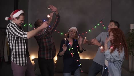 young aged people enjoying celebration, diverse young caucasian friends hanging out during the new year eve - dancing together with bengal lights inhands, having fun at home decorated with garland