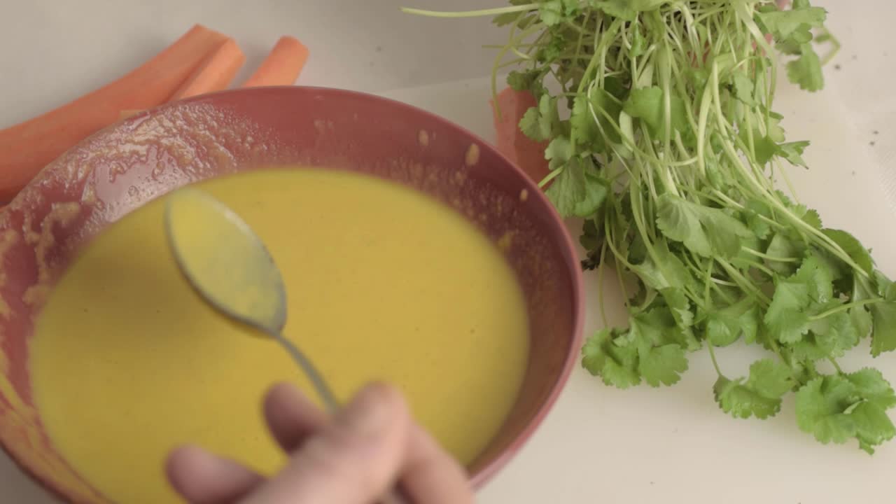 Hand stirring carrot and coriander soup with spoon