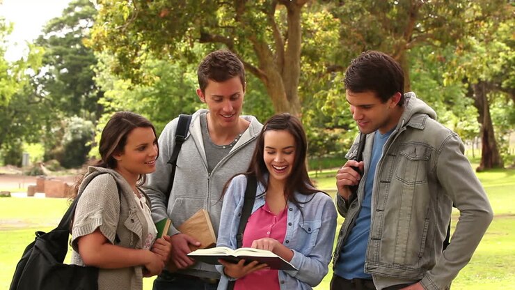 Quattro amici che ridono mentre indicano un libro, in piedi insieme in un parco.