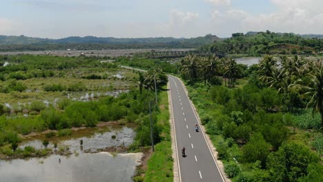 Aerial-view-trucking-shot,-motorcycle-moving-along-the-southern-road-of-Lombok,-bridge-and-river-in-the-background