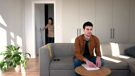 blind man reading a braille book sitting on sofa at home while his girlfriend bringing him a glass of water and helping him to drink