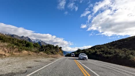 vehicles travel along a picturesque mountain road in queenstown, new zealand, under clear blue skies with scattered clouds