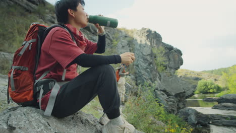 asian female hiker drinking water on river bank