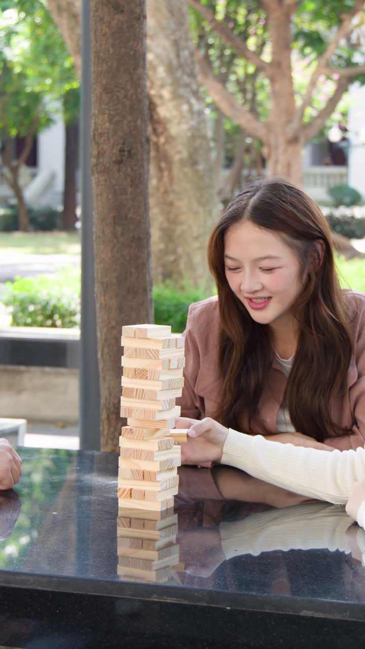 Un gruppo di giovani studenti thailandesi gioca a un gioco di blocchi di legno su un tavolo di pietra all'aperto.