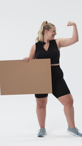 vertical video: flexing arm and smiling, plus size woman holding blank cardboard sign