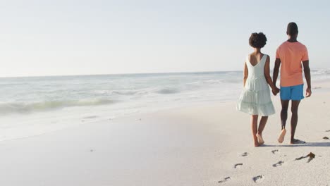 African-american-couple-holding-hands-and-walking-on-sunny-beach