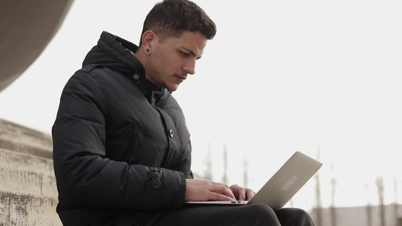 joven concentrado escribiendo en una computadora portátil mientras está sentado en las escaleras