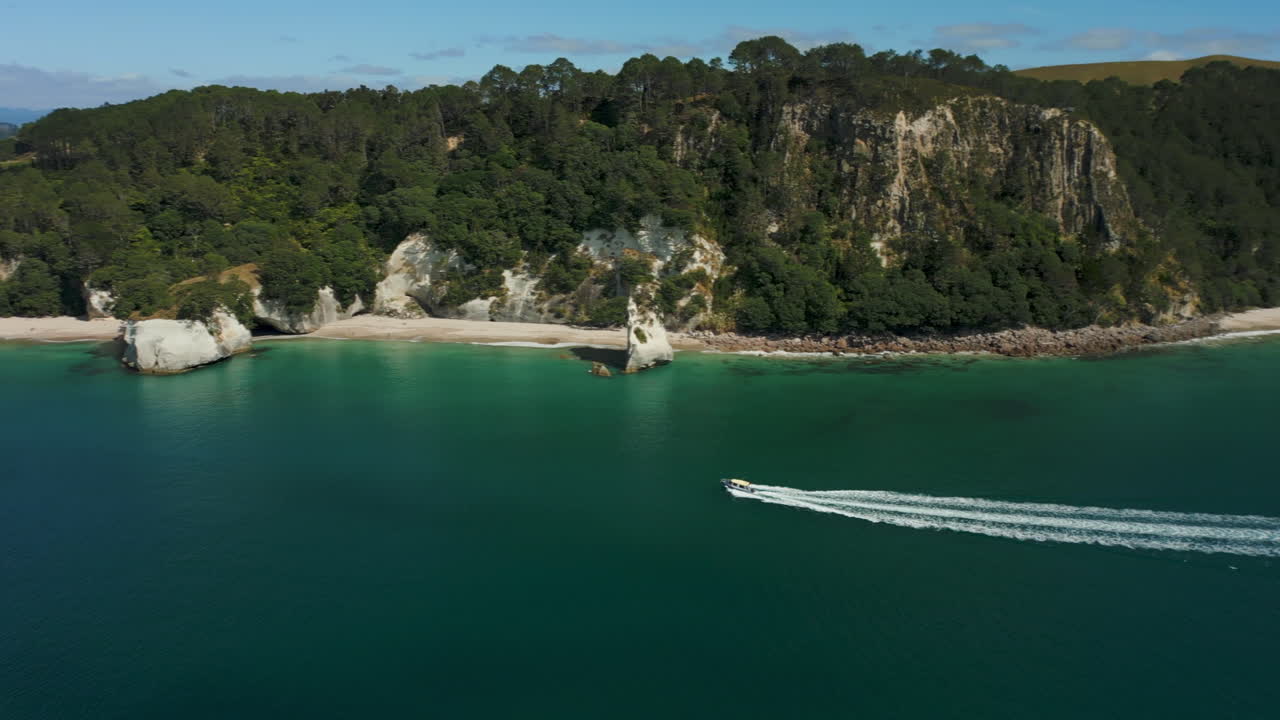un barco a motor trae turistas a te whanganui-a-hei o a la reserva marina de la bahía de la catedral - paralaje aéreo
