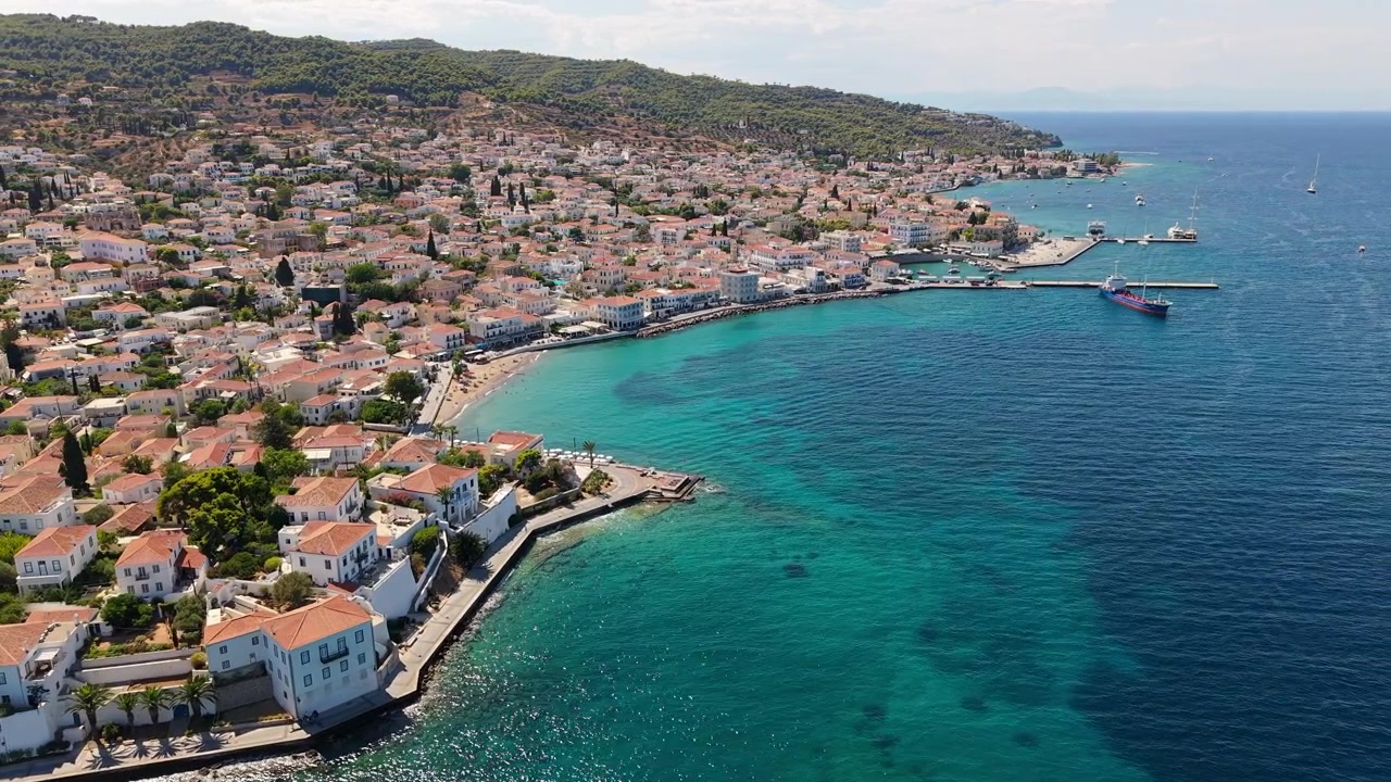 I tetti in terracotta e le eleganti dimore neoclassiche della città di Spetses digradano verso una costa turchese brillante. Il porto di Dapia e le colline ricoperte di pini si estendono su quest'isola greca cosmopolita