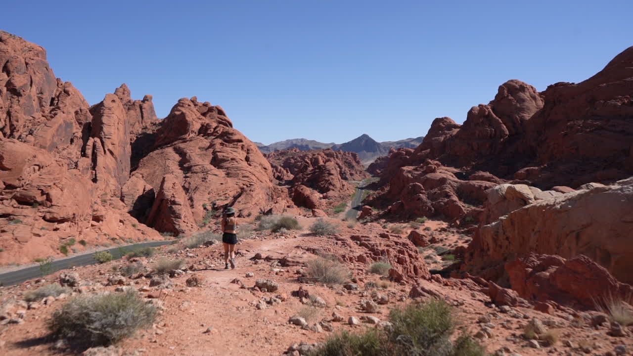 parte posterior de la mujer caminando por la carretera en el paisaje de roca arenisca roja del valle del fuego, nevada usa, cámara lenta de marco completo