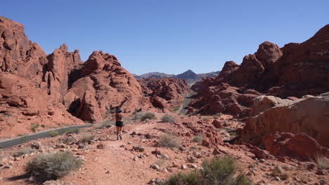 Rückseite-Der-Frau,-Die-An-Der-Straße-In-Roter-Sandsteinfelsenlandschaft-Des-Tals-Des-Feuers,-Nevada,-USA,-Vollbild-Zeitlupe,-Spazieren-Geht