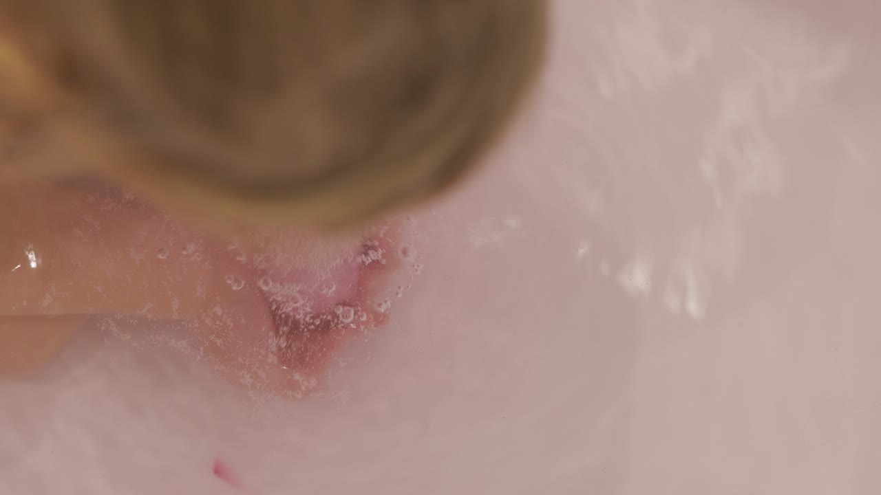 Mani di una bambina mettono una bomba da bagno nell'acqua. La palla di sale da bagno si dissolve.