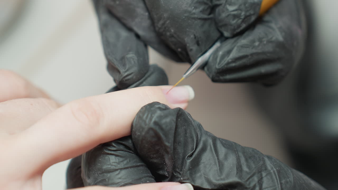 Close-up of nail technician wearing black glove using fine brush to fill nail polish carefully onto client fingernail, showcasing precision and attention to detail during manicure procedure