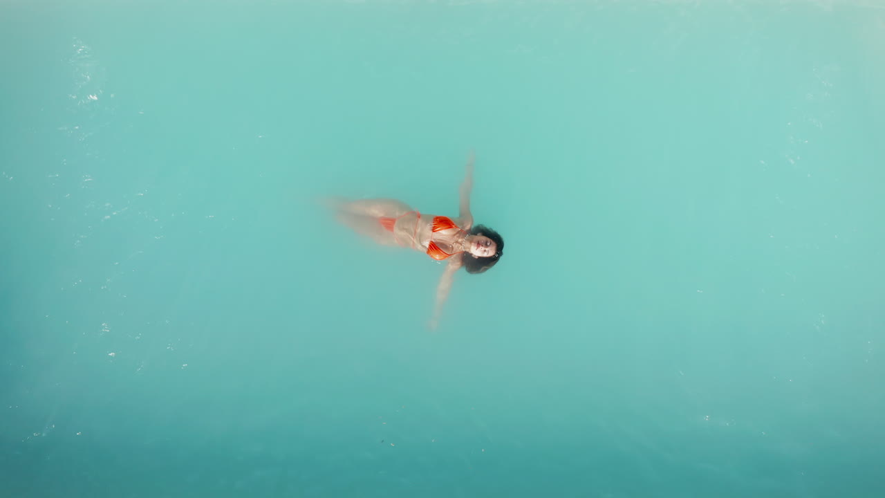 Aerial top down close up view beautiful girl in red bikini float on turquoise water on holiday relaxing vacation. Crystal clear turquoise sea. Vacation travel at Paradise