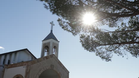 church bell tower with a white cross next to tree, low angle