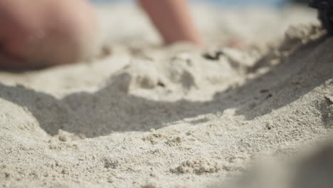 boy's hands pushing a small toy tractor along the sandy beach