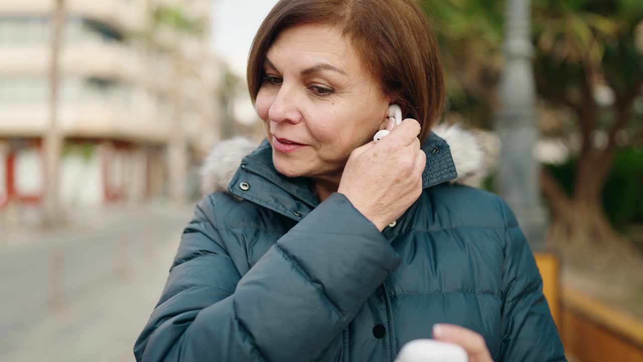 mujer de mediana edad sonriendo confiada guardando auriculares en la calle