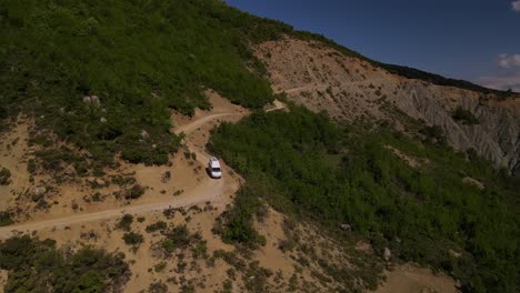 Drohnenaufnahmen-Eines-Weißen-Wohnmobils,-Das-Den-Berghang-Trebešinë-dëmbel-nemerçkë-In-Der-Nähe-Von-Permet,-Albanien,-Hinunterfährt