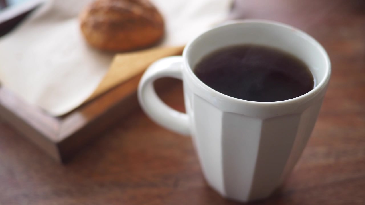 Caffè caldo fumante in una tazza bianca con un dolce su un tavolo di legno