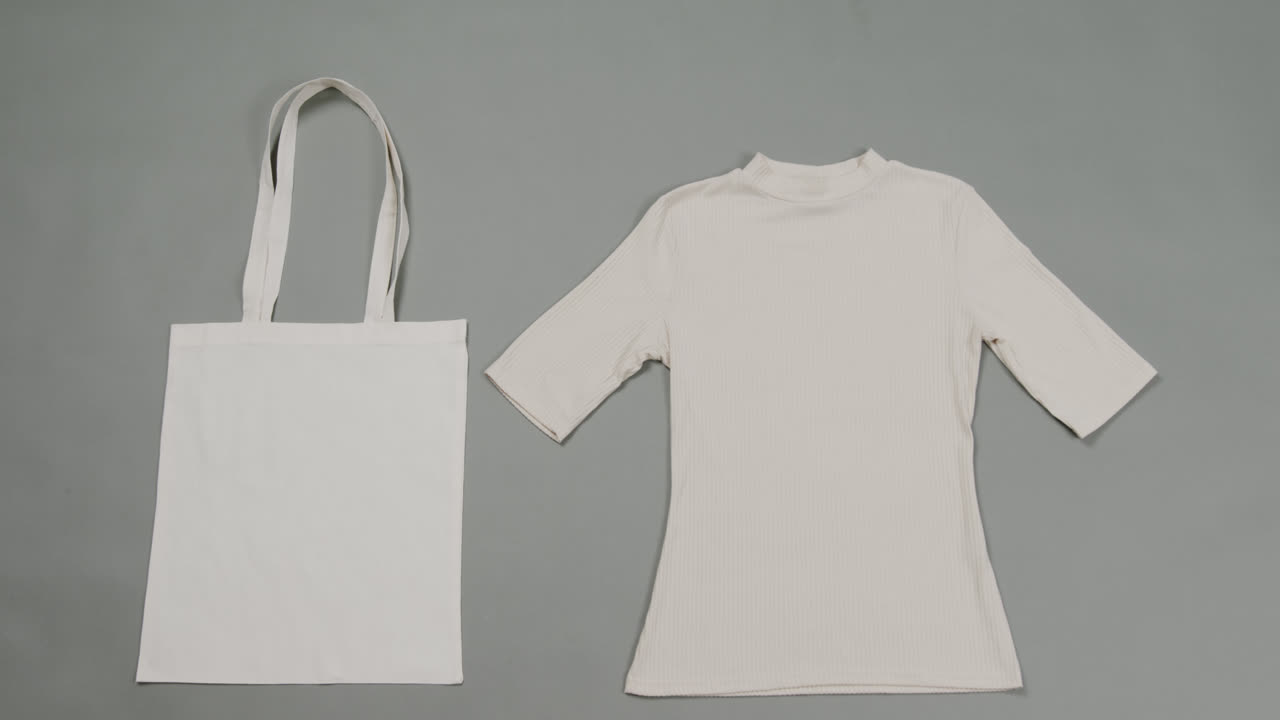 primer plano de una bolsa blanca y una camiseta sobre un fondo gris, con espacio de copia, cámara lenta