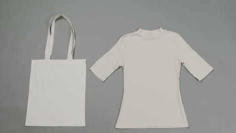 Close-up-of-white-bag-and-t-shirt-on-grey-background,-with-copy-space,-slow-motion