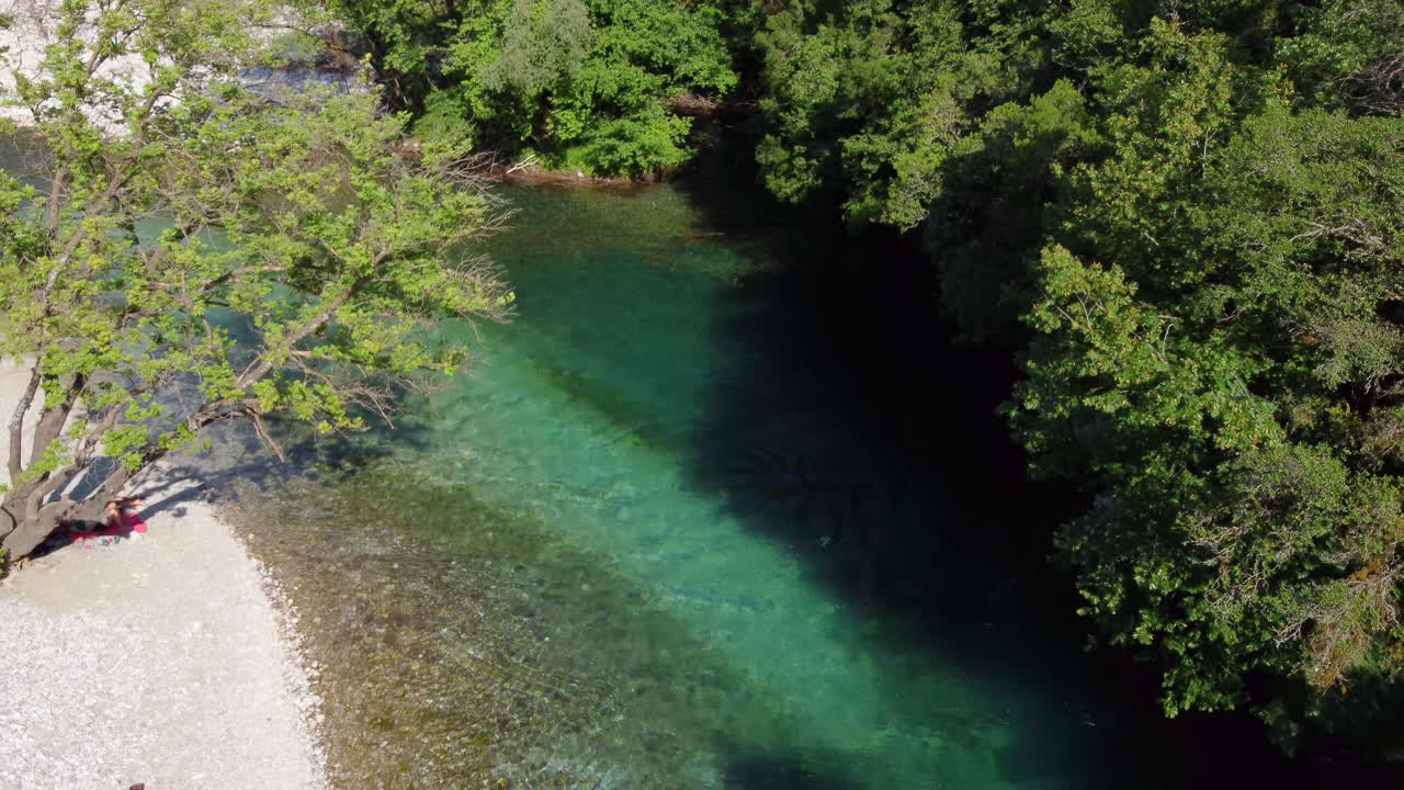 Una donna si gode il sole mentre è sdraiata sulla riva ciottolosa del famoso fiume Voidomatis che scorre attraverso il Parco Nazionale del Vikos in Epiro, Grecia.