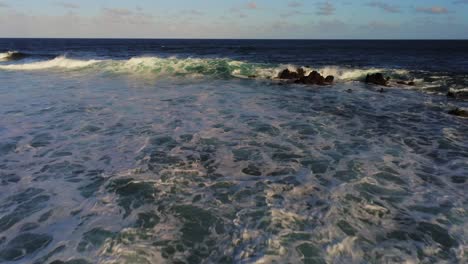 vibrant blue ocean waves hitting rocky coastline and breaking on shallow coast, aerial view