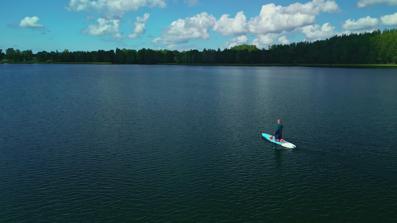 un hombre solitario está serenamente navegando, capturando recuerdos inolvidables en un lago tranquilo y azul profundo envuelto en una exuberante vegetación verde que ofrece sentimientos abrumadoramente intensos