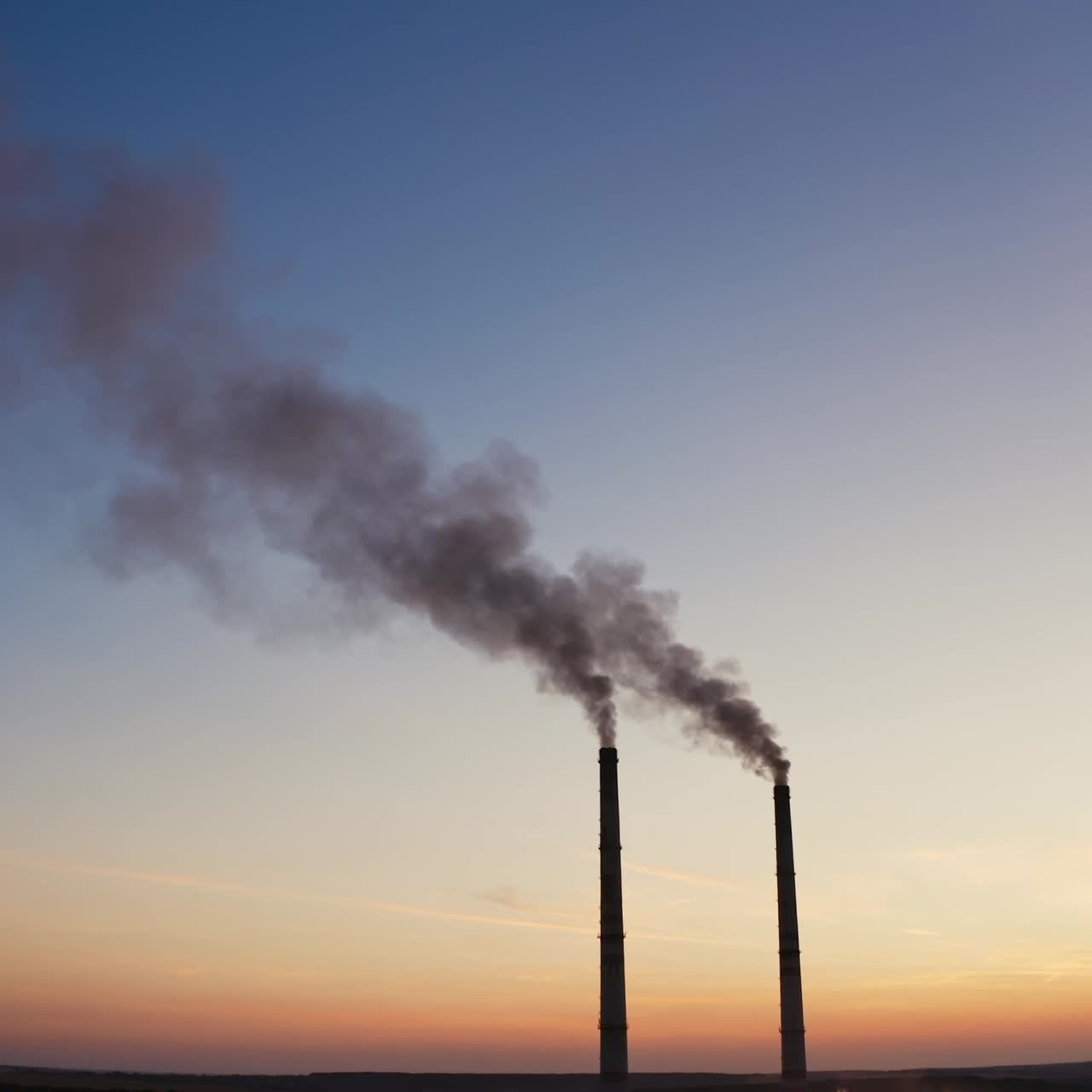 Pollution of the environment.Toxic smoke going from two pipes of a factory on the evening sky background at sunset.