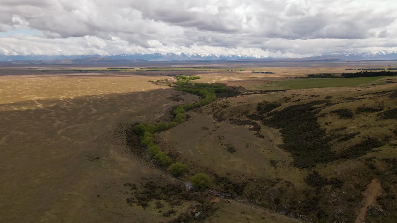 antena - cauce de un río con frondosos árboles serpenteando a través de un paisaje montañoso seco con montañas cubiertas de nieve en el fondo