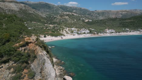 Sideways-reveal-shot-of-Albanian-Livadi-beach-in-front-of-mountain-landscape