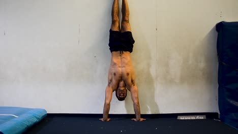 a still shot of a shirtless muscled guy doing handstands in gymnastics gym