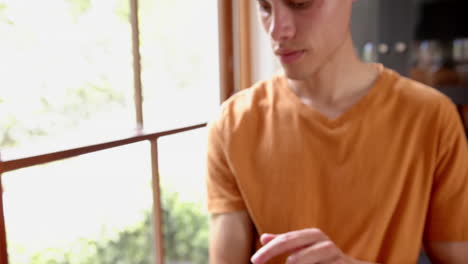 thoughtful biracial man using tablet by window in living room, copy space, slow motion