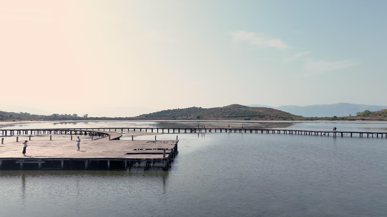 일몰 동안 바다 위의 나무 다리를 걷고 플랫폼에서 사진을 찍는 사람들