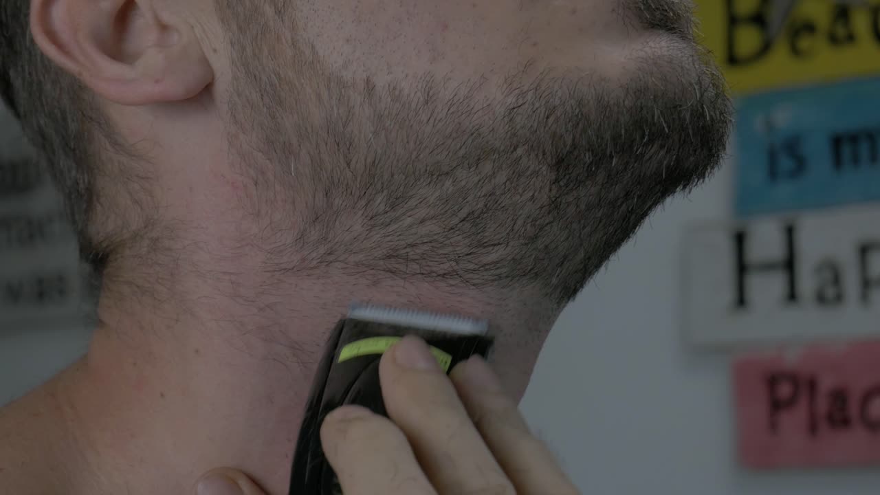 hombre caucásico afeitando su barba a cero longitud de cabello con afeitadora eléctrica