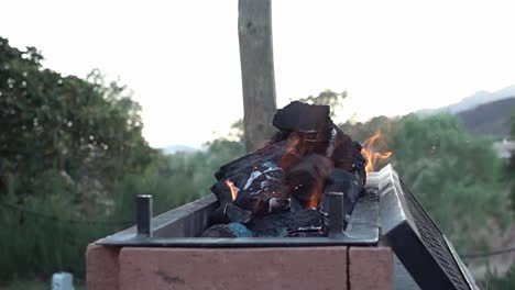 Slow-motion-shot-of-woodturning-black-within-a-firepit-with-flames-and-smoke-rising