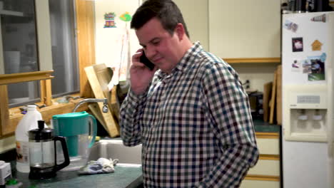 hombre tomando una llamada telefónica informal en su celular en la cocina