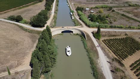 drone-shot-of-a-bridge-on-The-canal-Du-Midi-France,-walkways-on-both-side-of-the-canal-with-vineyards