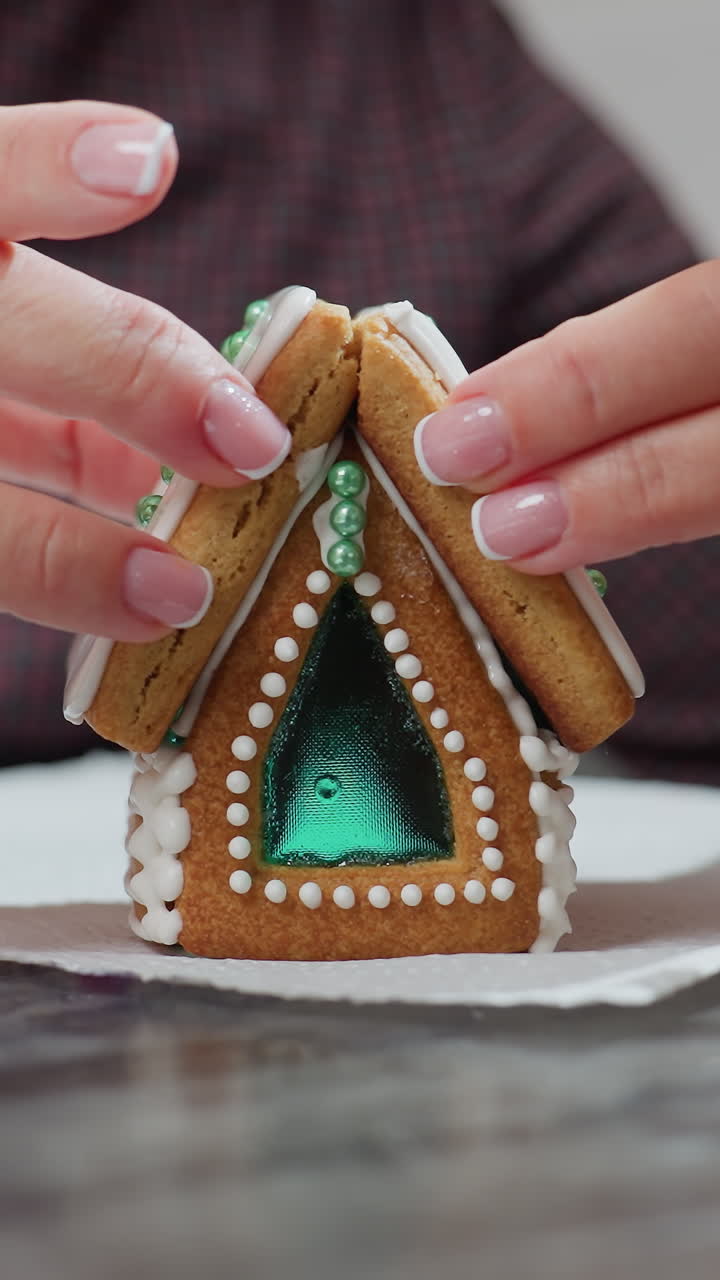 신선한 아이싱과 복잡한 장식으로 새로 조립된 진저브레드 하우스 쿠키를 안정시키는 캐터러의 클로즈업