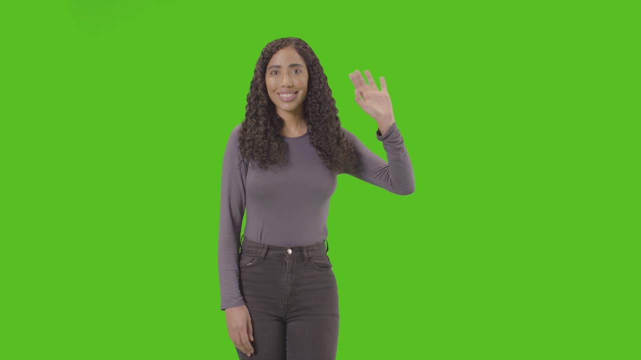 Studio Three Quarter Length Shot Of Woman Waving At Camera Against Green Screen