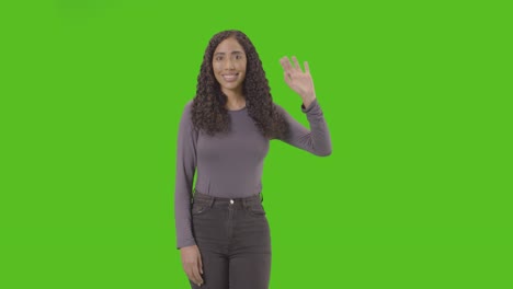 foto de estudio de tres cuartos de longitud de una mujer saludando a la cámara contra una pantalla verde