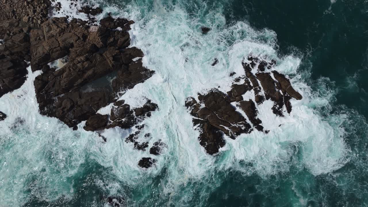 Veduta aerea a volo d'uccello che mostra l'aspro affioramento roccioso circondato da onde che si infrangono a Playa Chica, situata a Quintay, Casablanca, Valparaíso, Cile. Ripresa in discesa