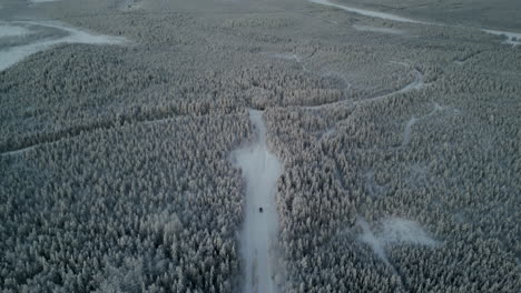 drone footage captures a black van moving through a snow-covered forest in luosto, finland, near the arctic circle, as it descends