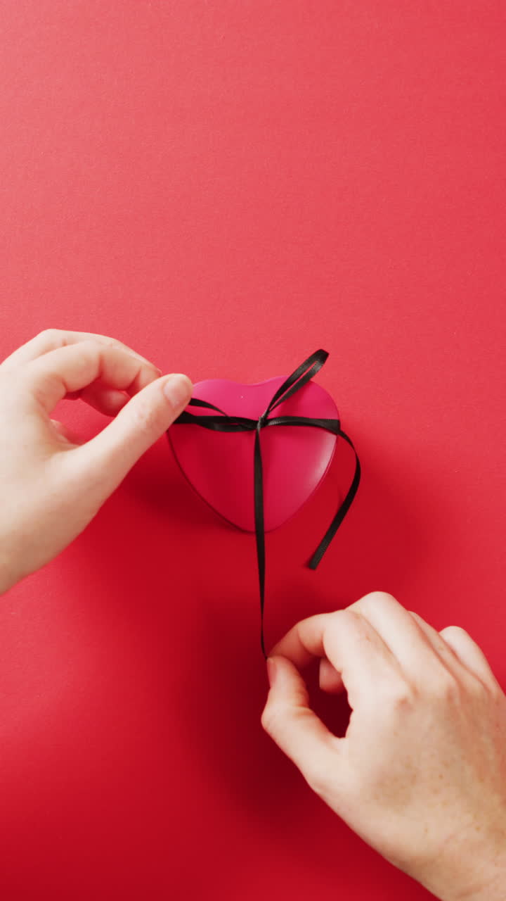 빨간색 심장 모양의 상자에 리본을 는 손의 수직 비디오, 복사 공간과 함께 빨간색 배경