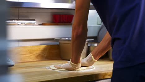 professional chef kneading floured dough for bread in bakery shop. man`s hands are forming the dough on a floured surface and kneading it with his hands.