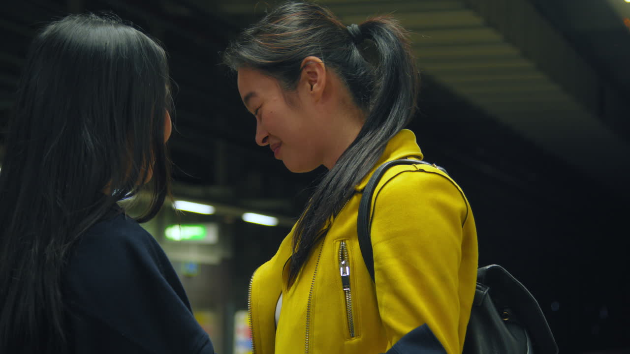 두 젊은 여자 친구가 지하철역 플랫폼 2에서 작별 인사를 하고 안고 있다.