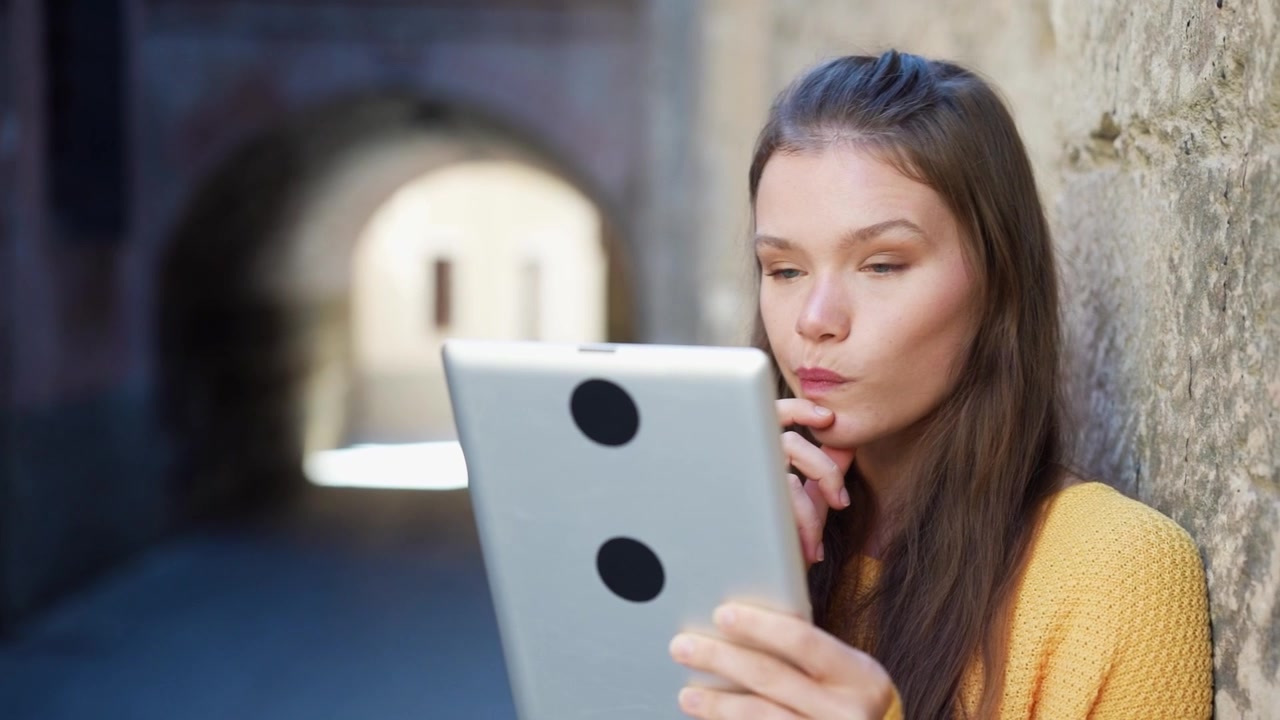 Eine junge Frau benutzt ein Tablet in einer lebhaften urbanen Umgebung bei natürlichem Tageslicht.