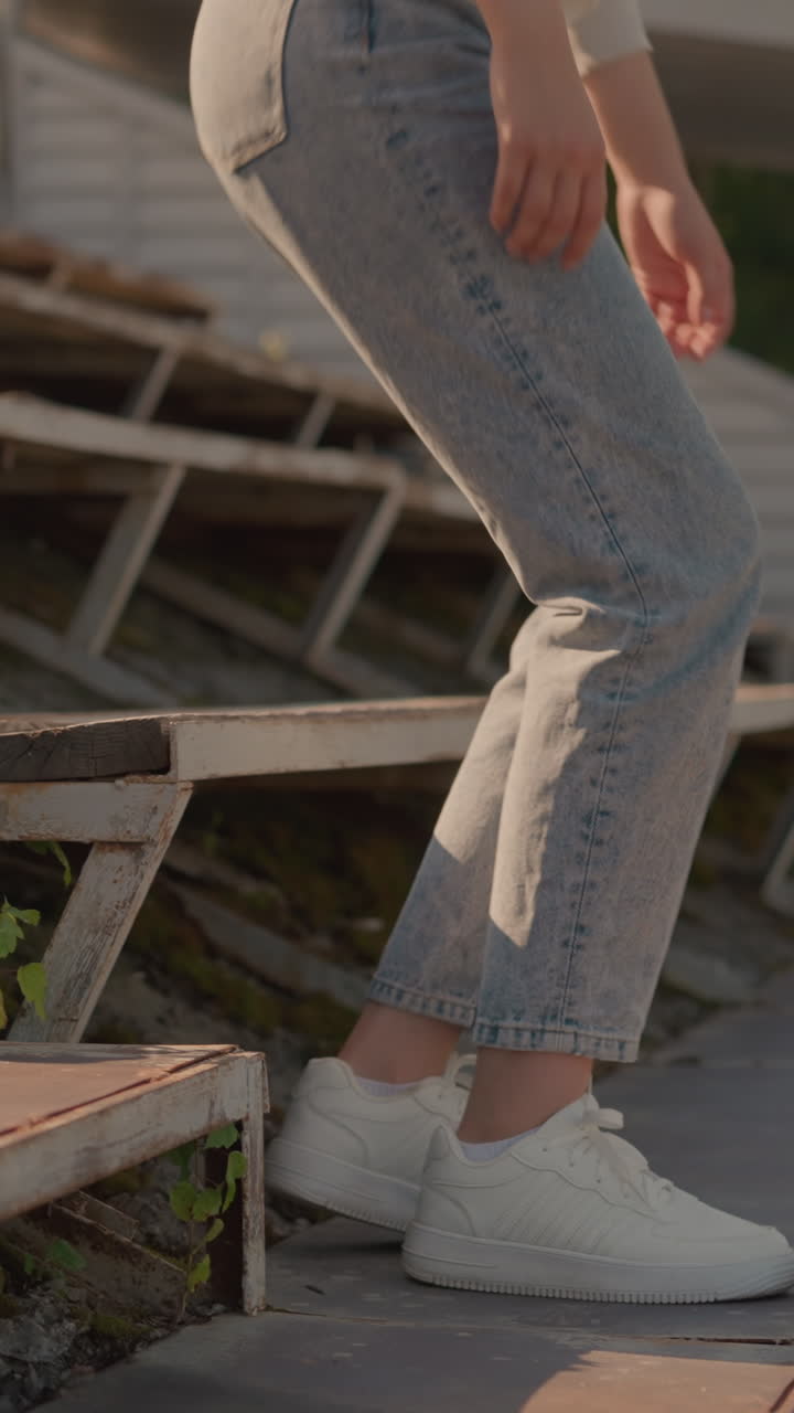 Close-up of girl s legs as she steps up rustic stadium seating, she sat on the first roll, with visible greenery growing among rusty seat frames, background shows blurred greenery