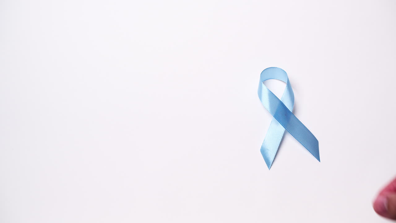 Dettaglio di mano maschile che posiziona un nastro di colore azzurro chiaro su sfondo bianco