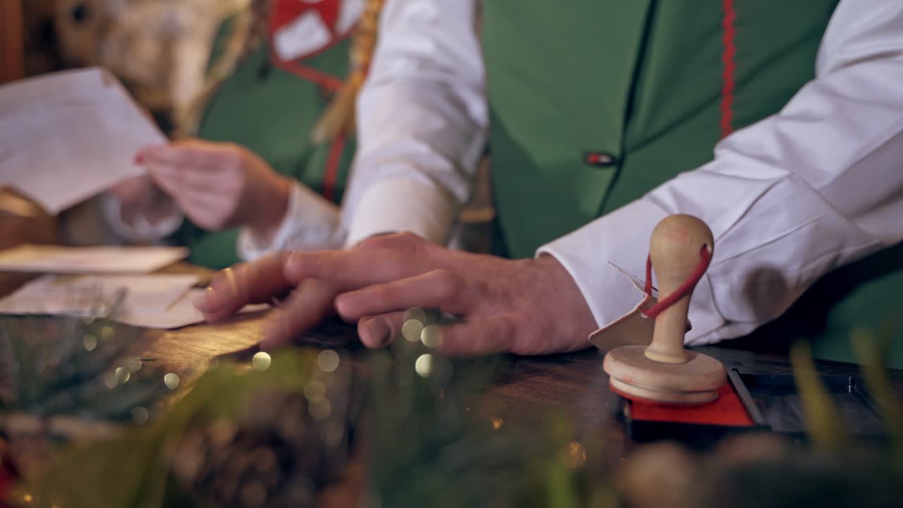 Envelopes on the table for Christmas. Fairy elf puts seal on envelopes. Quick motion. Close-up hands with signet.